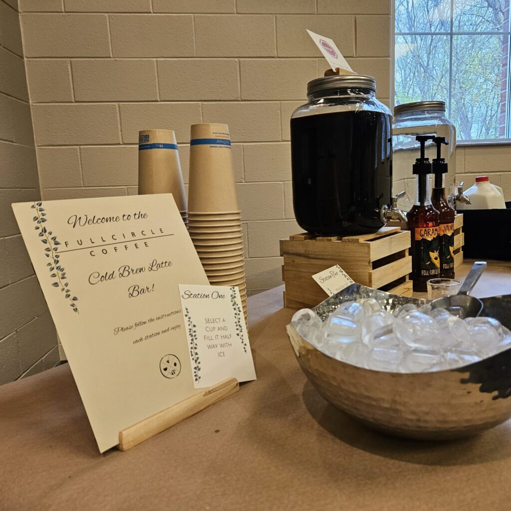 A cold brew latte bar setup for a wedding shower, featuring coffee dispensers, flavor syrups, ice, cups, and elegant signage.