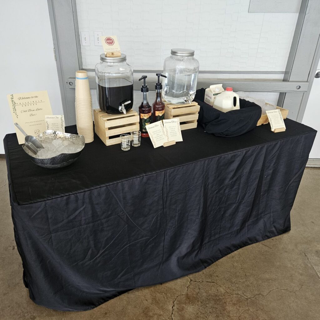 A cold brew latte bar setup featuring coffee dispensers, flavor syrups, ice, and cups, prepared for a graduation party.