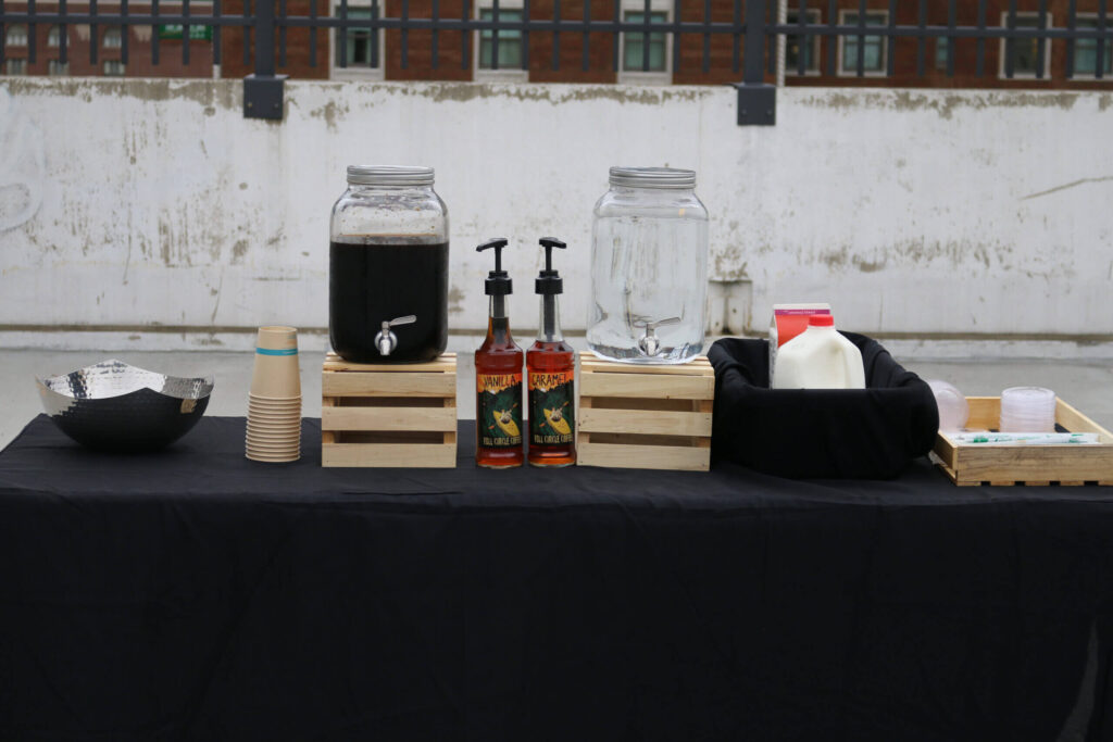 A cold brew latte bar setup with dispensers for coffee and water, flavor syrups, milk, and serving accessories, ready for a catered event.