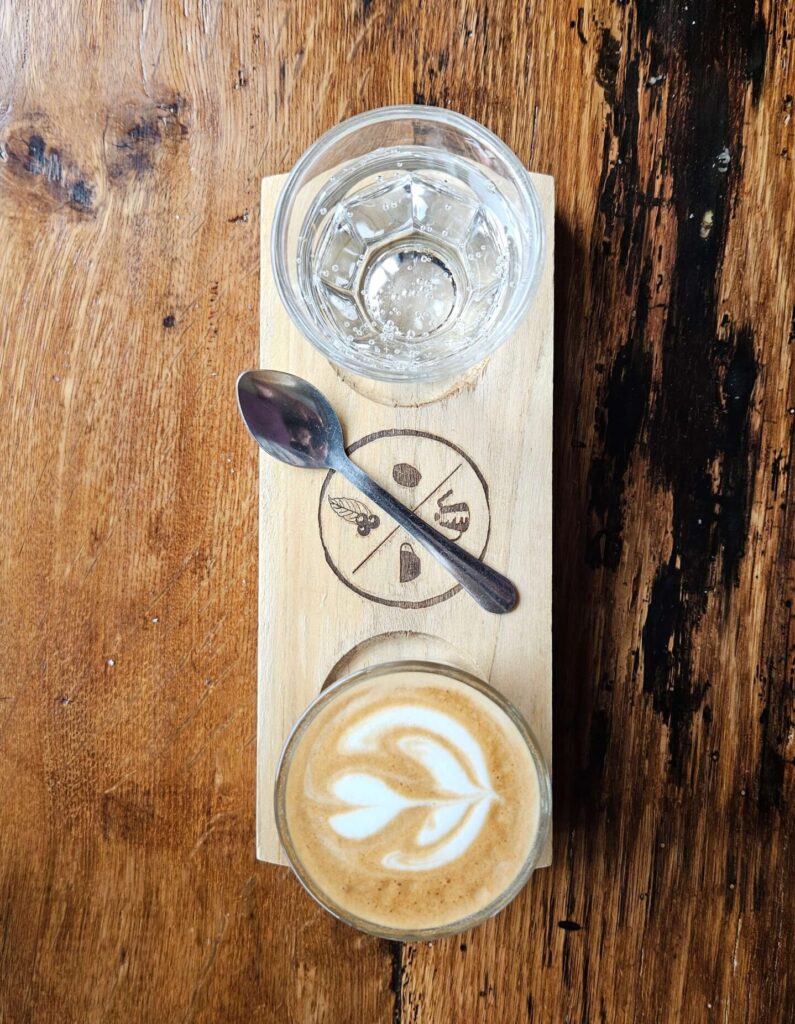 A beautifully crafted cortado with latte art, served on a wooden tray with a glass of sparkling water and a spoon, placed on a rustic wooden table at Full Circle Coffee in West Michigan.